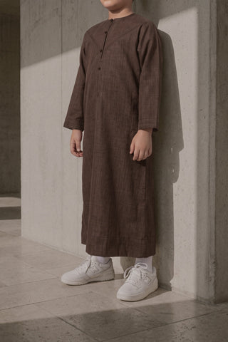 Brauner Qamis für Jungen vor einer Betonwand